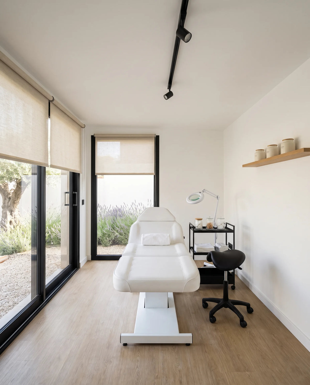 Visualización de un NOOK 10 preparado para tratamientos faciales, con una camilla reclinable, una lámpara de trabajo y luz de día en el vidrio
