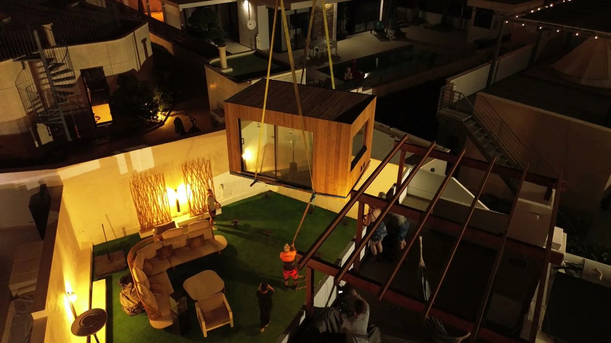 A crane lowers a finished NOOK 10 into a private home at night.